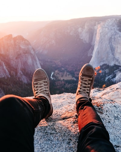 人穿着棕色系带运动鞋坐在石山白天
